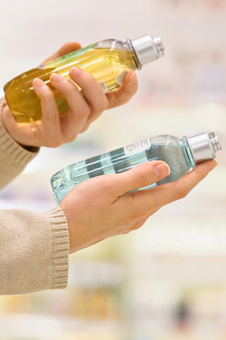 Vertical shot: Woman reading the label of a cosmetic product in a store aisle, focusing on ingredients, with shelves and bottles in the background