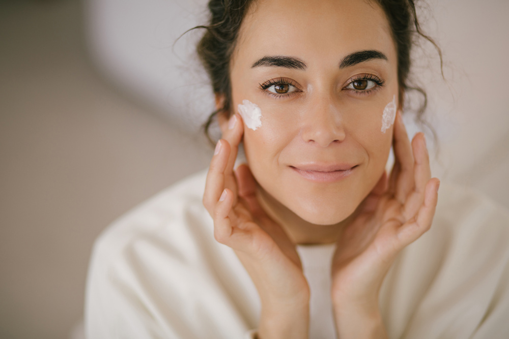 Young woman 30 years old applying face cream on her skin. Close up portrait