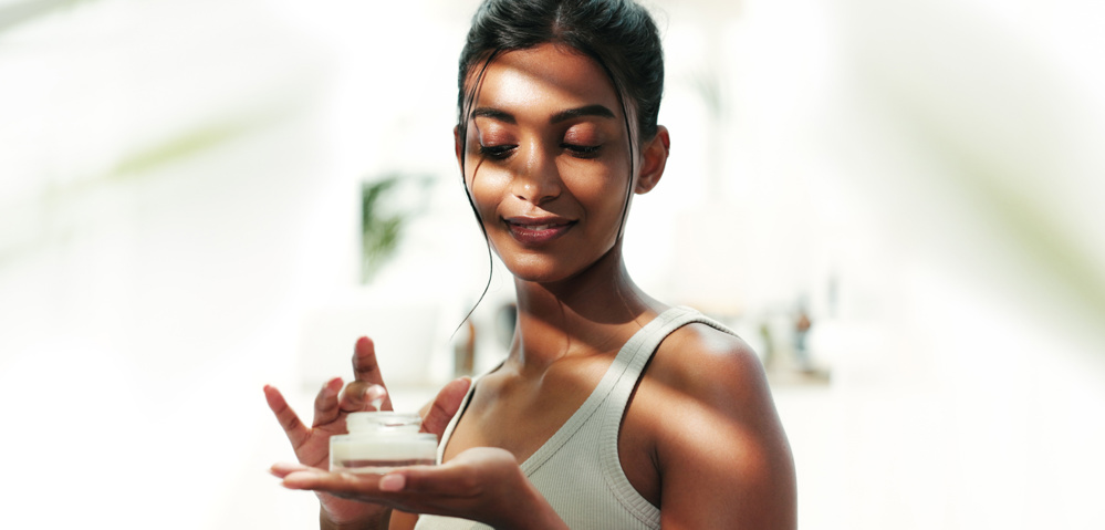 Bathroom, woman and apply with cream for skincare, wellness and anti-aging benefits for self-care. Home, female person and cosmetics product with smile for moisturizer, lotion and sunscreen treatment